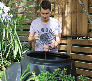 a man using a Compost Mate tool to stir and mix organic materials inside a compost bin