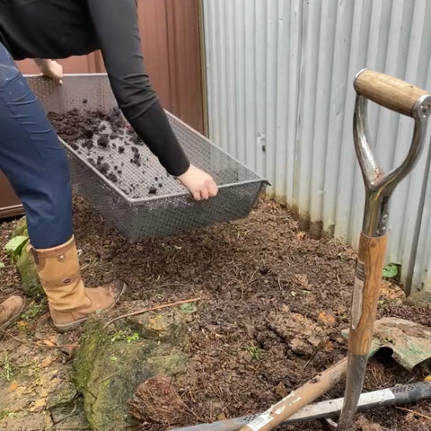 a person holding a metal bin with dirt and shovel