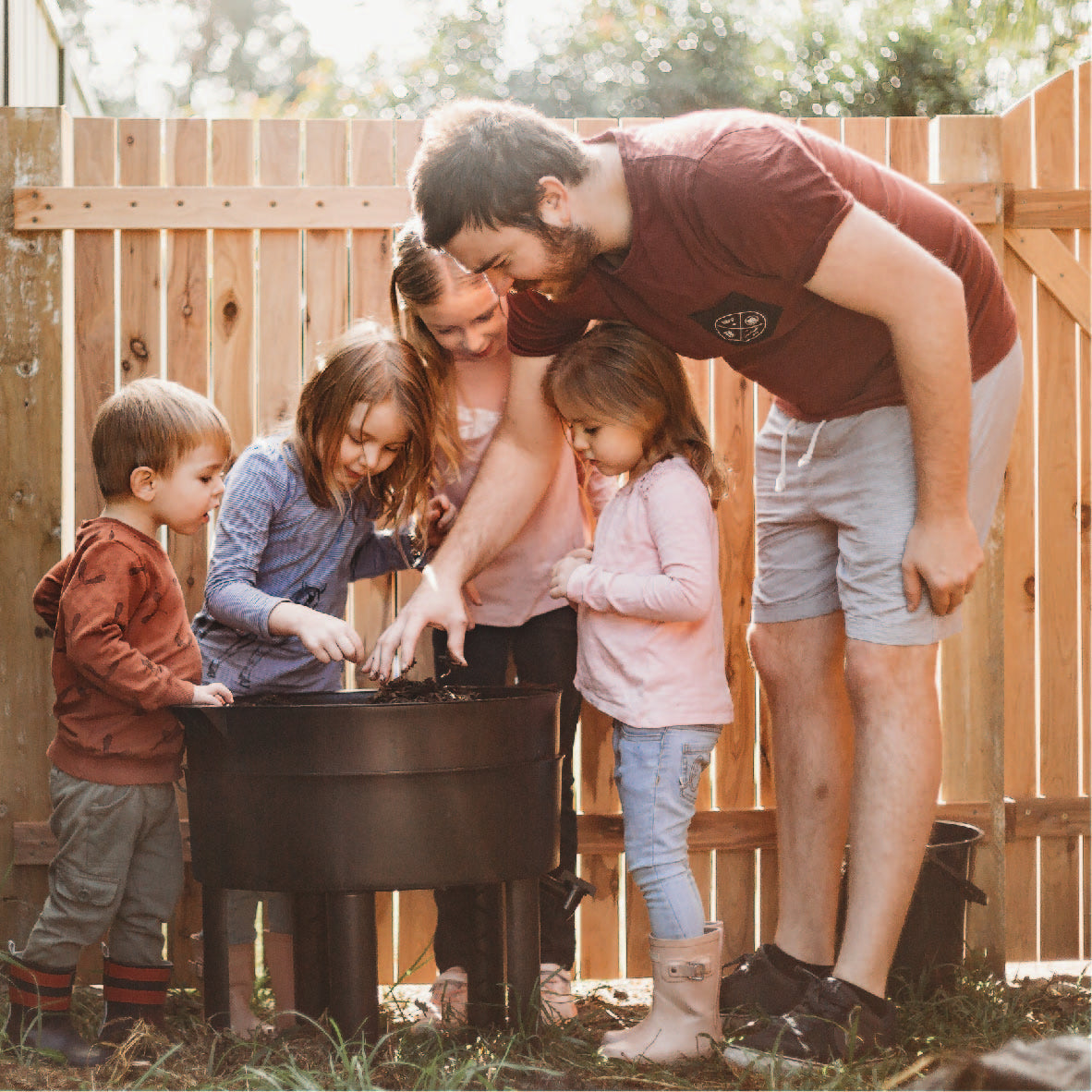 a father with his kids standing around a black worm farming tub